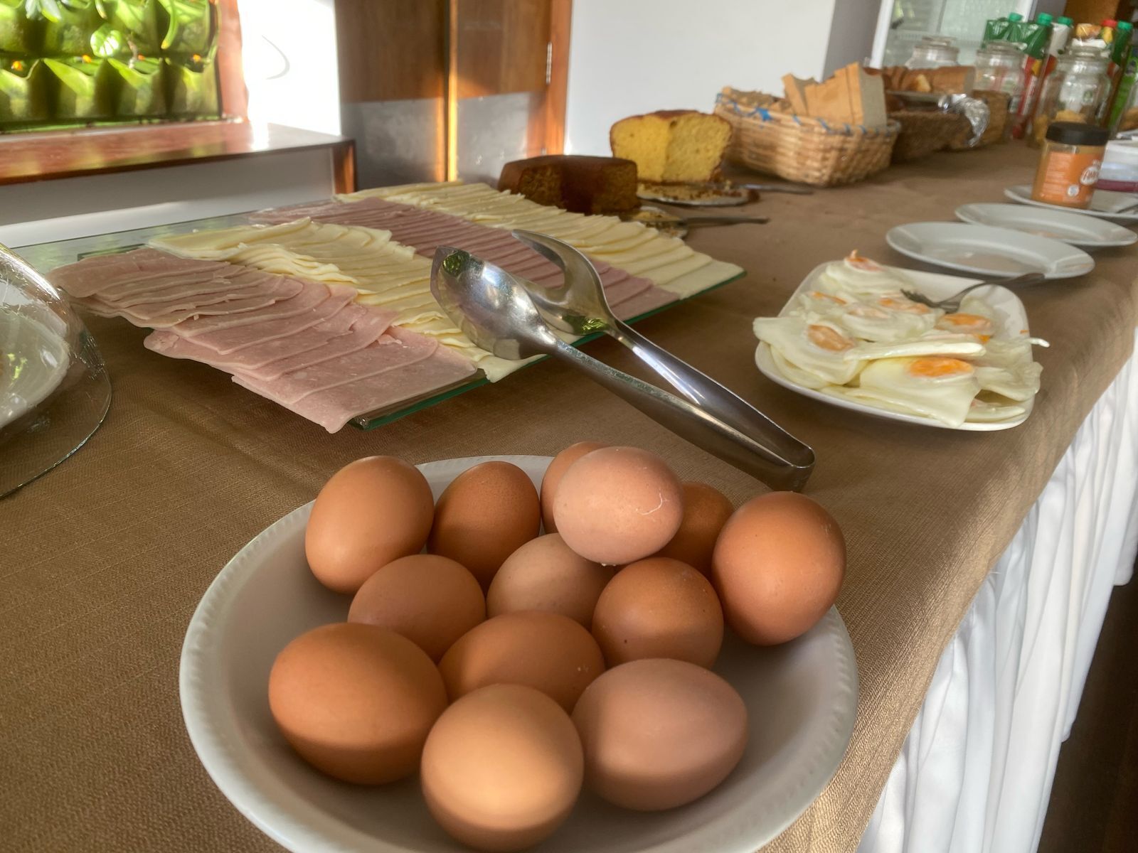 Une table de buffet proposant divers aliments, notamment des œufs, du jambon et du pain.