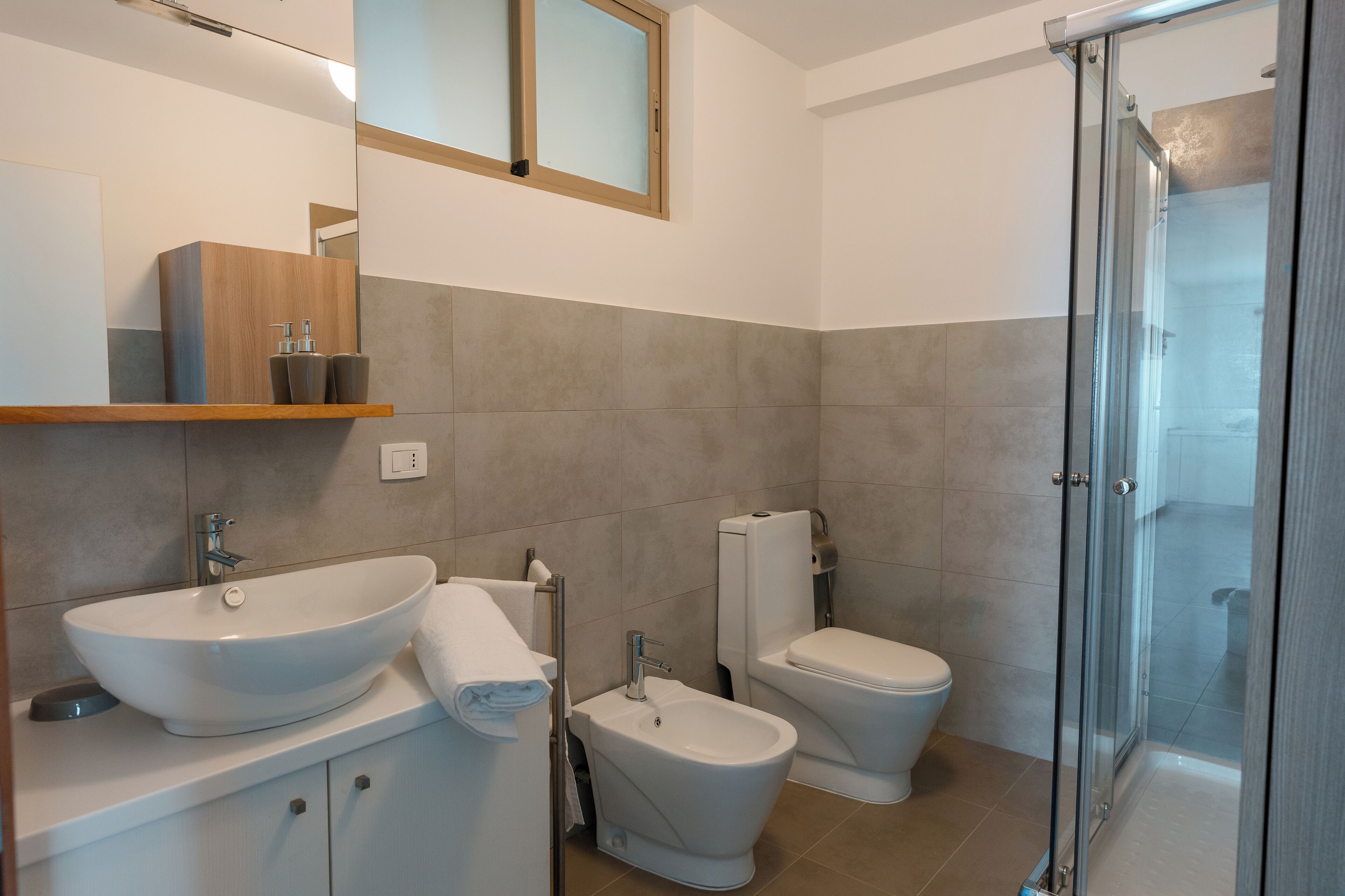 A modern bathroom with a large vessel sink, a bidet, a toilet, and a glass-enclosed shower.