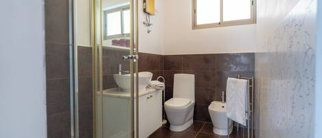 Een moderne badkamer met een douchecabine van glas, een wit wastafelmeubel, een toilet en een bidet.
