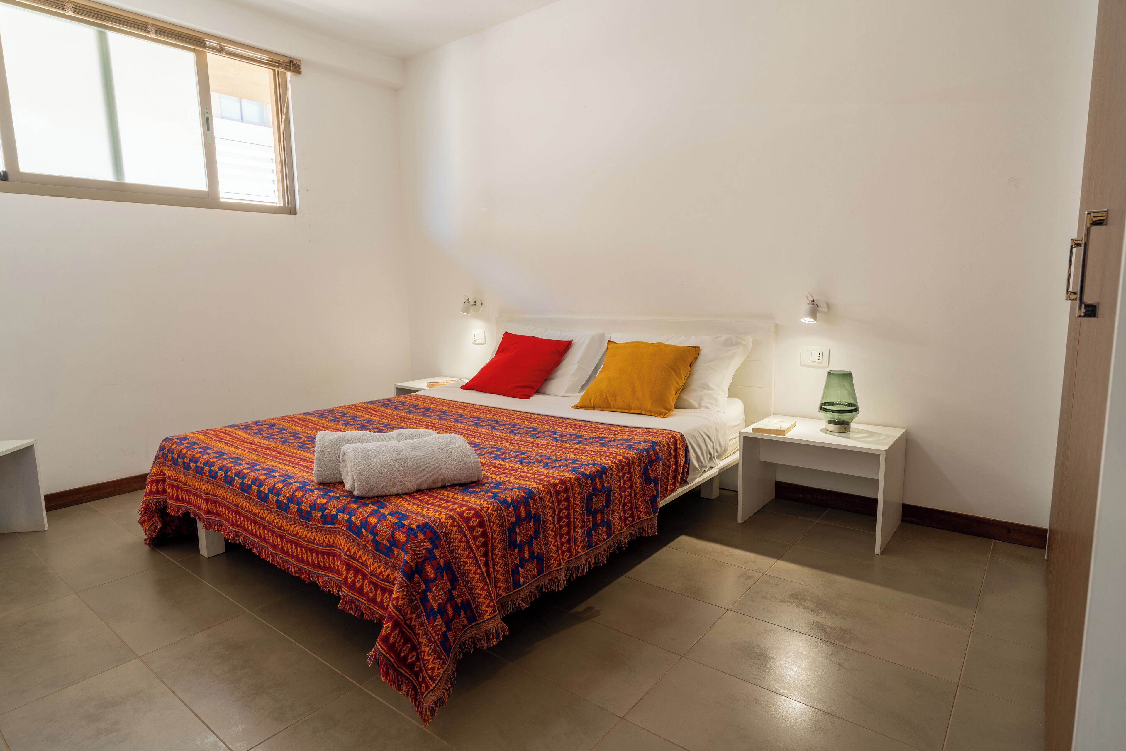 Un dormitorio ordenado con cama, mesitas de noche y una ventana.