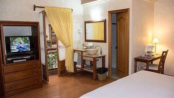 A hotel room with a bed, a TV, a bathroom with a mirror, and a desk with a chair.