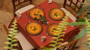 Mesa para cuatro personas con mantel rojo y platos naranjas, rodeada de sillas de madera.