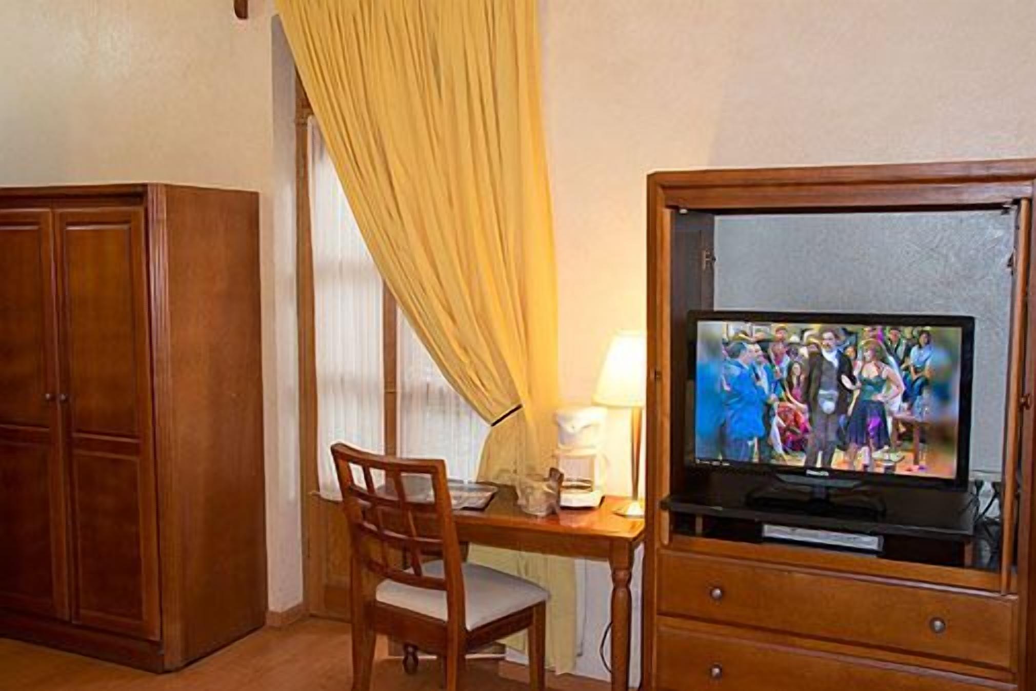 A hotel room with a wooden desk, a television, and a wardrobe.