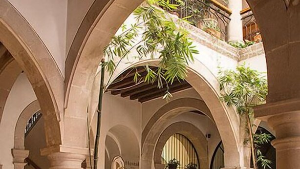 A spacious atrium with high stone arches, a staircase, and multiple potted plants. - Hostal De La Monja (Durango)