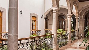 A corridor with arches, columns, and a tiled floor, featuring wooden doors and metal railings. - Hostal De La Monja (Durango)