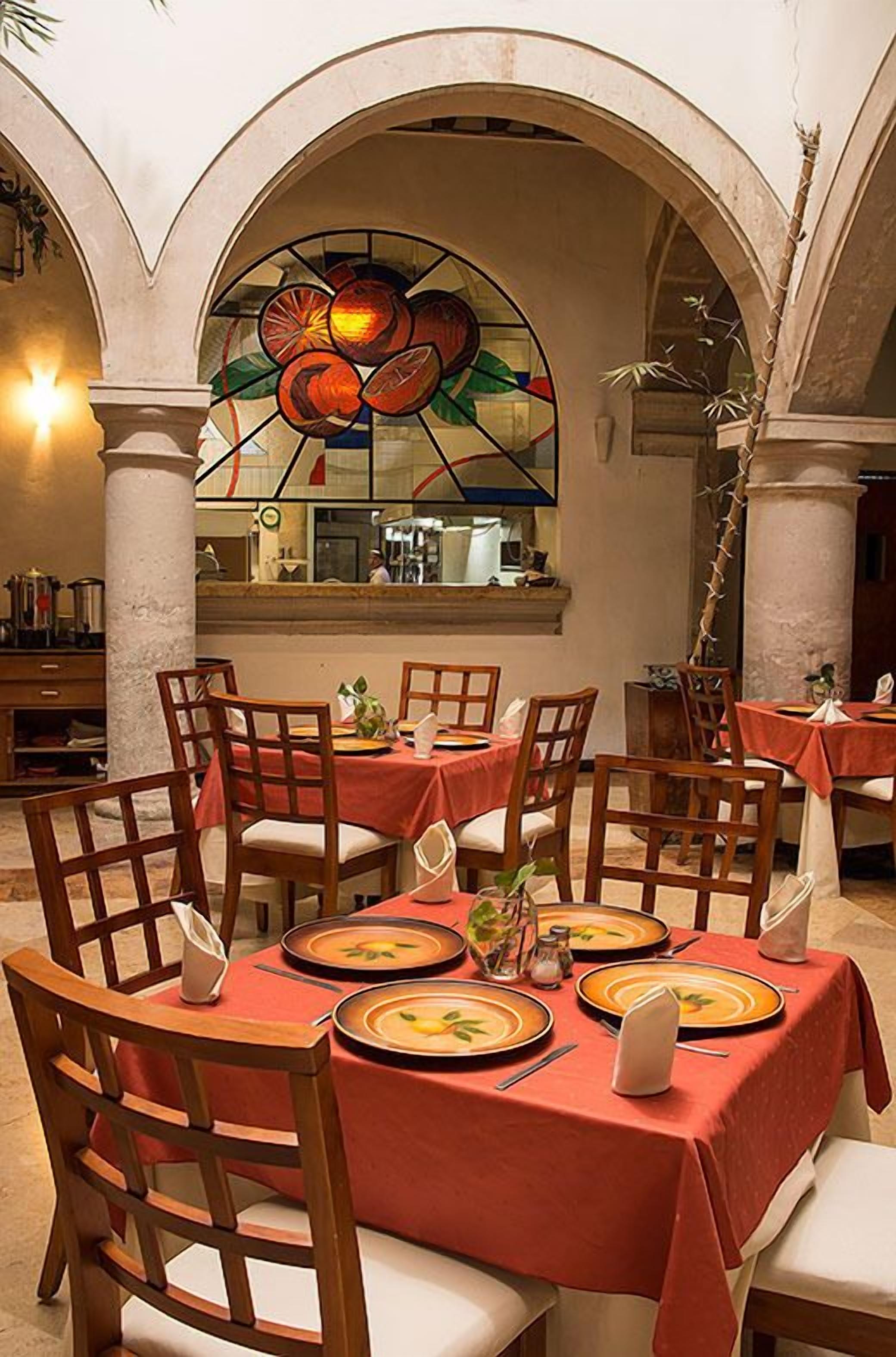 A restaurant with tables set for dining, featuring a stained glass window with fruit design.