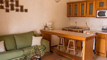 A compact kitchen with wooden cabinets, a central island with stools, a green sofa, and a small potted plant.