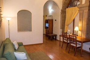 Ein gemütliches Wohnzimmer mit einem grünen Sofa, einem Holzesstisch mit Stühlen, einem Fernseher und einer Lampe.