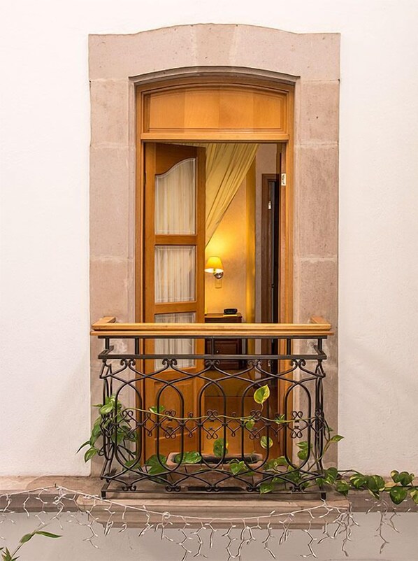 A wooden door with a glass panel, a small balcony with a wrought iron railing, and a potted plant. - Hostal De La Monja (Durango)