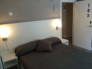 Une chambre d’hôtel avec un lit, deux lampes de chevet, une table de nuit et une porte portant le numéro 103.