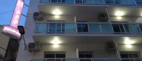 A multi-story hotel with balconies, air conditioning units, and a neon sign.
