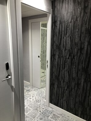 Un pasillo con baldosas de diseño, una puerta blanca y una pared oscura con textura.