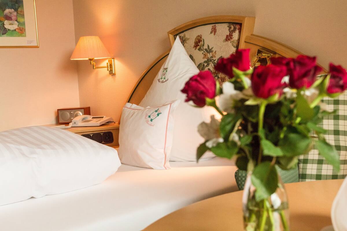 Una habitación de hotel con una cama bien hecha, una lámpara de noche, un teléfono y una almohada estampada con flores.