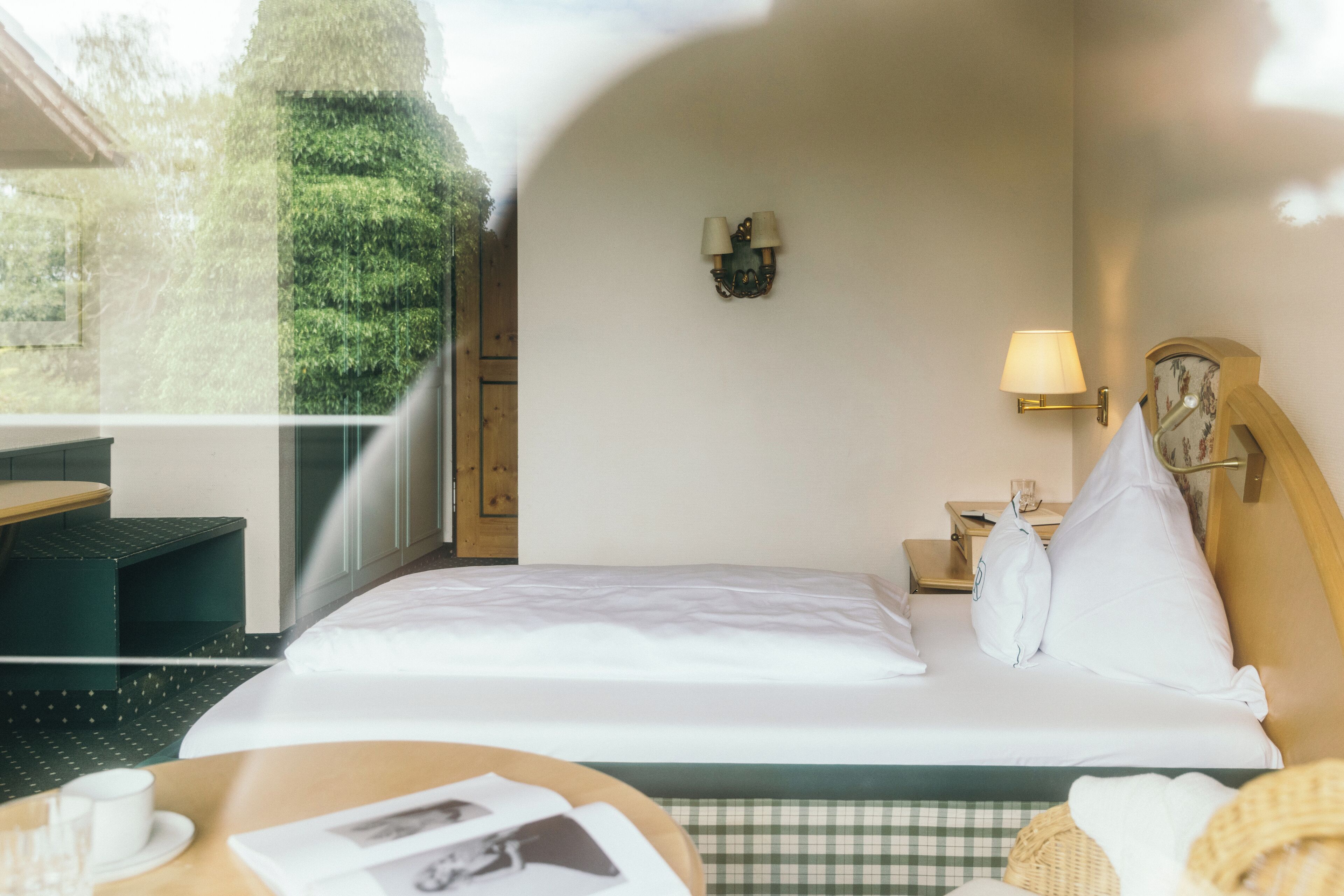 Ein Hotelzimmer mit Bett, Nachttisch, Lampe und Blick auf Grün.