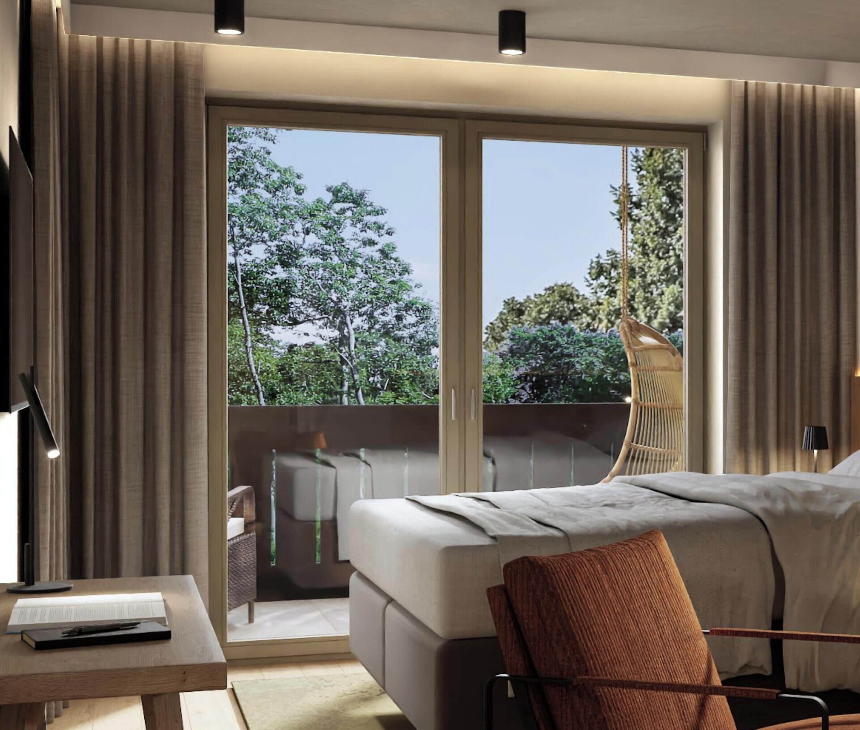 A modern hotel room with a bed, a chair, a table with a book, and a view of trees through large windows.