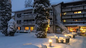 A snow-covered outdoor area with tables and chairs, a building with multiple floors, and a staircase leading to the upper levels. - Garden Hotel Reinhart (Prien am Chiemsee)