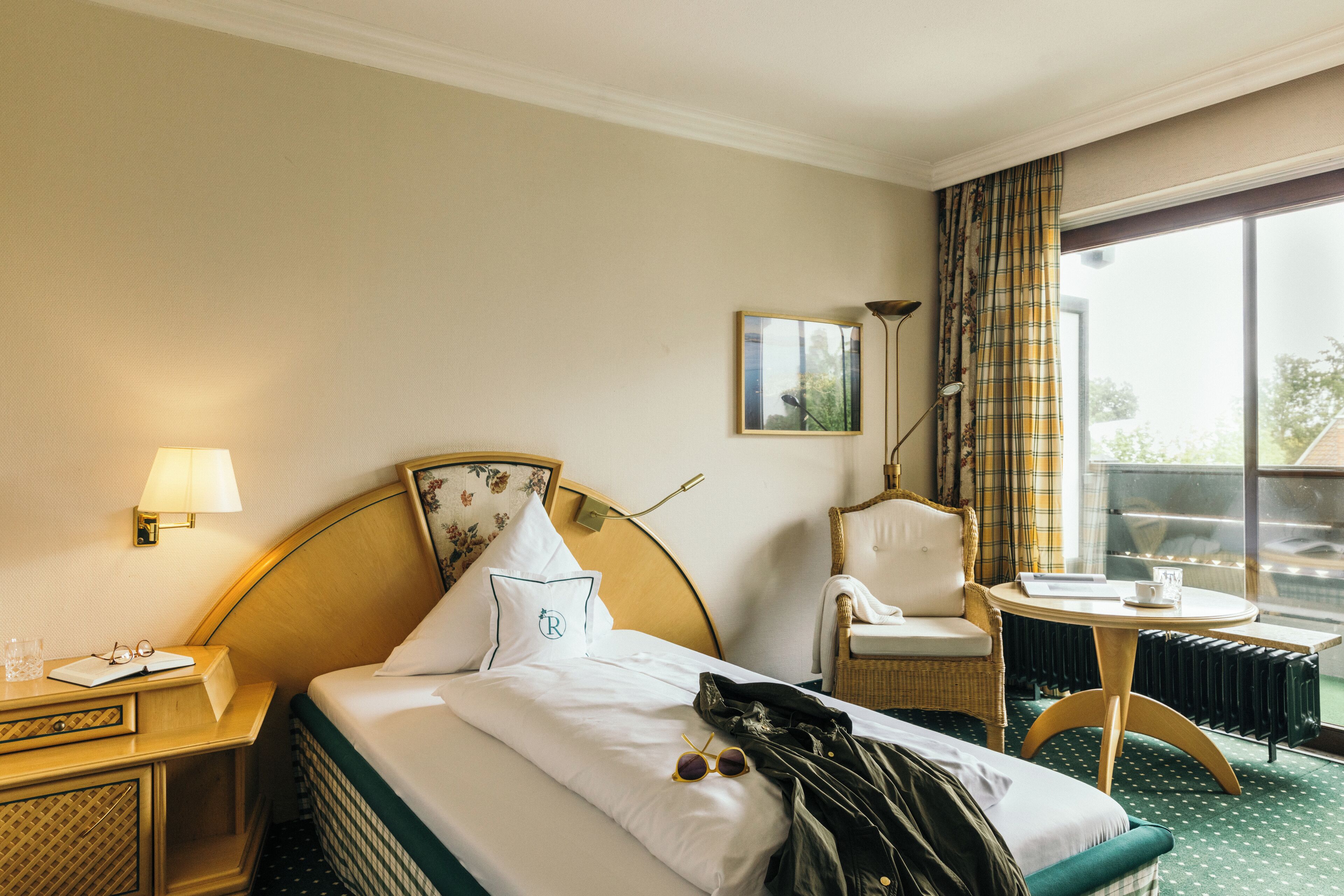 A hotel room with a bed, a chair, a table, and a window with curtains.