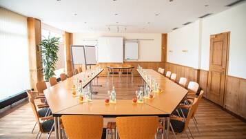 A conference room with a long table, chairs, whiteboards, and a potted plant.