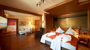 A hotel room with a wooden floor, a bed with white linens, a wooden wardrobe, a small armchair, and a painting on the wall.