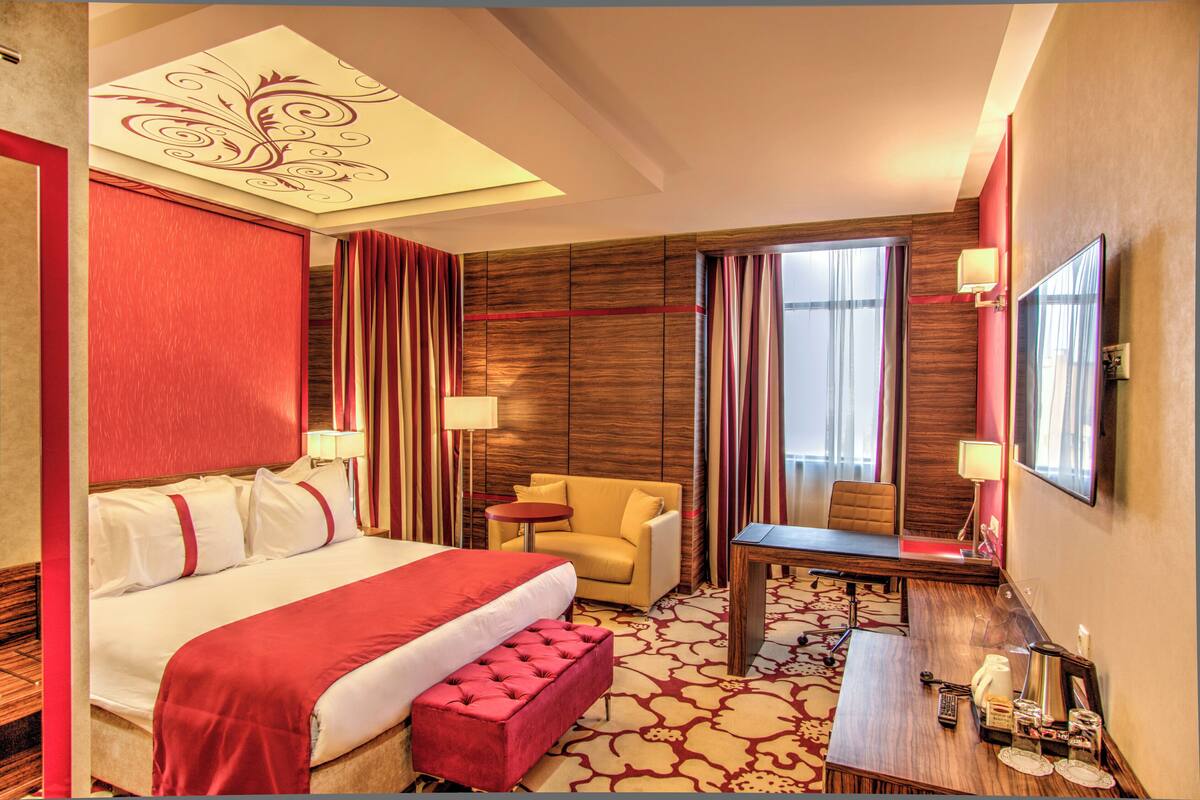 A hotel room with a large bed, a desk, a chair, and a television.