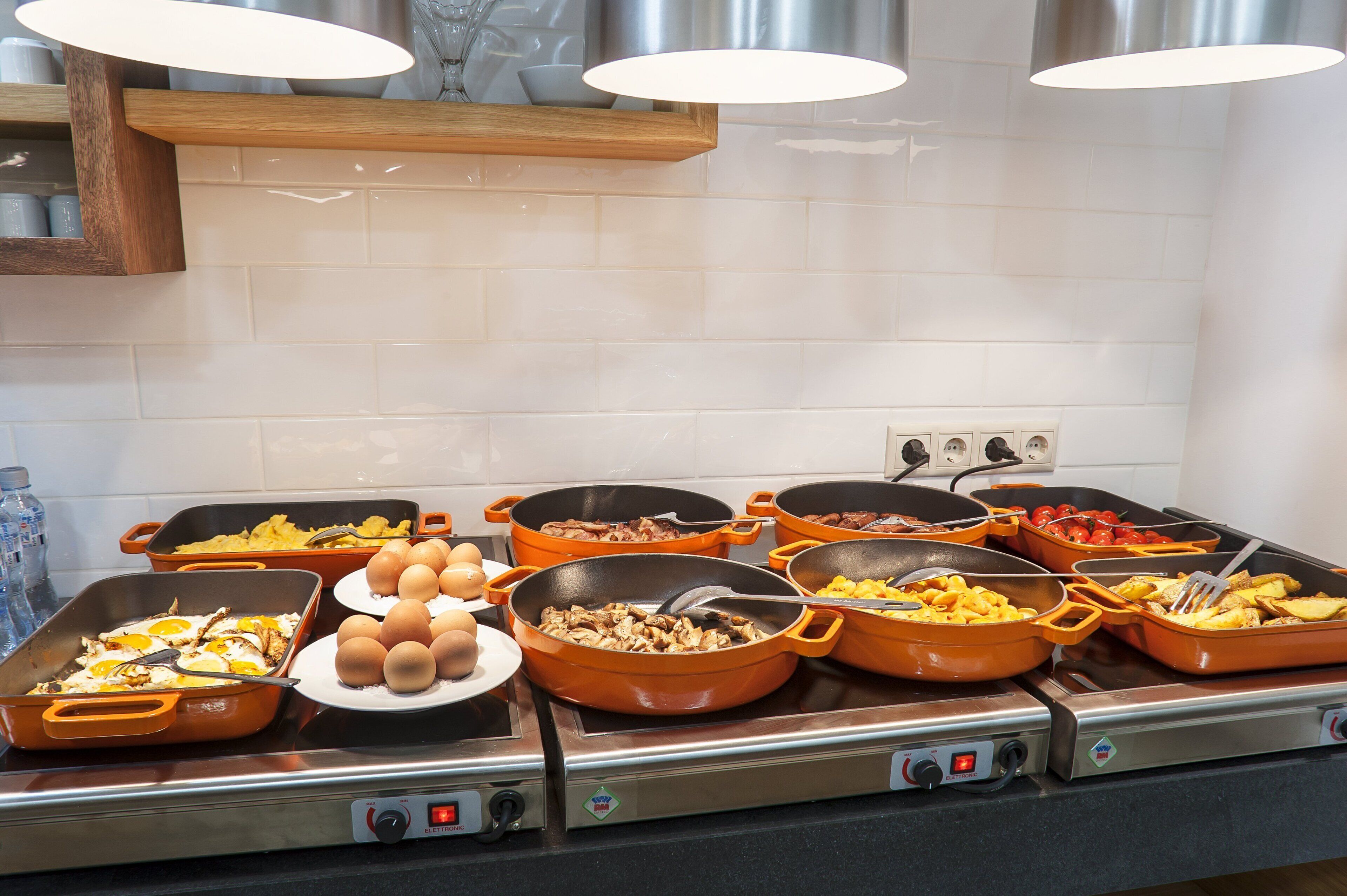 A buffet with various dishes in orange pans, including eggs, meats, and vegetables.