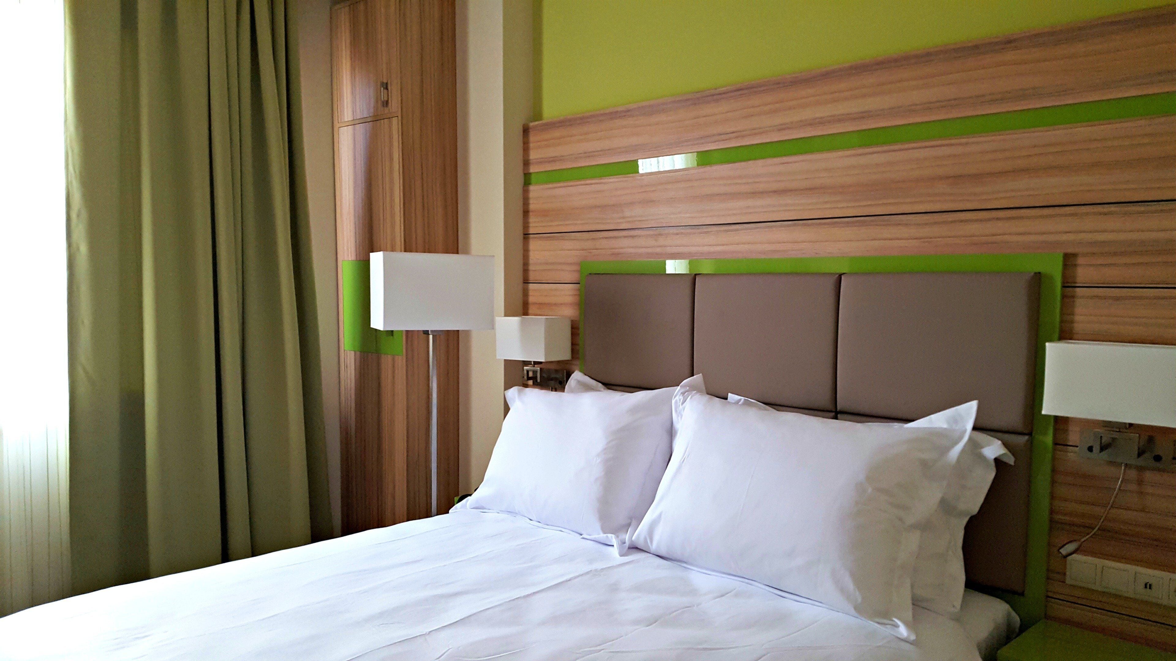 Ett hotellrum med en säng, två sänglampor och en grön accentvägg.