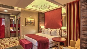 A hotel room with a large bed, a bedside table, a chair, and a small desk with a lamp. - Holiday Inn Plovdiv by IHG (Plovdiv)