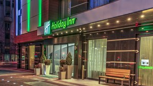 A Holiday Inn hotel with a modern facade, large glass windows, and a bench outside. - Holiday Inn Plovdiv by IHG (Plovdiv)