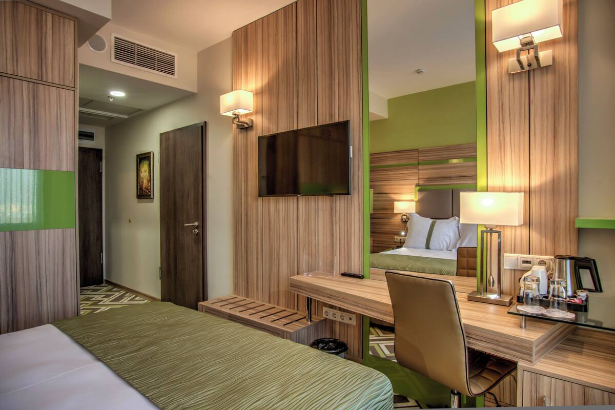 A hotel room with a bed, desk, chair, TV, and a mirror.