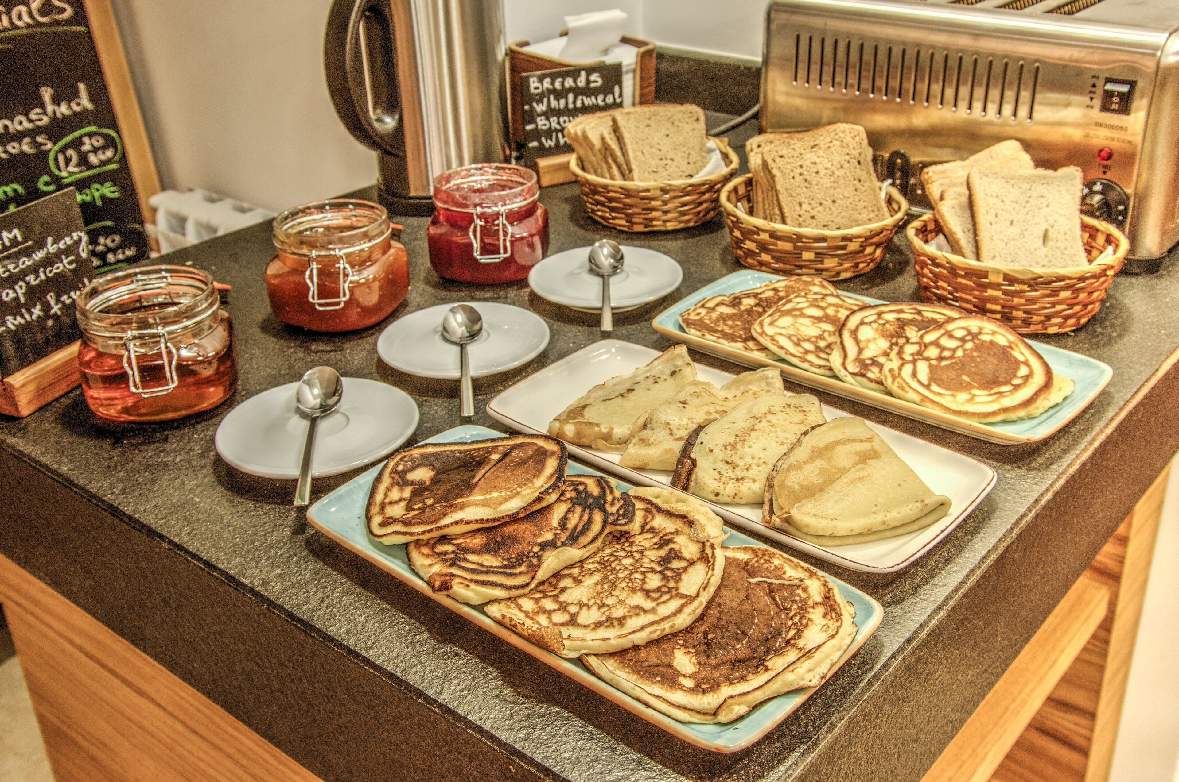 A breakfast buffet with various food items including pancakes, bread, and jams.