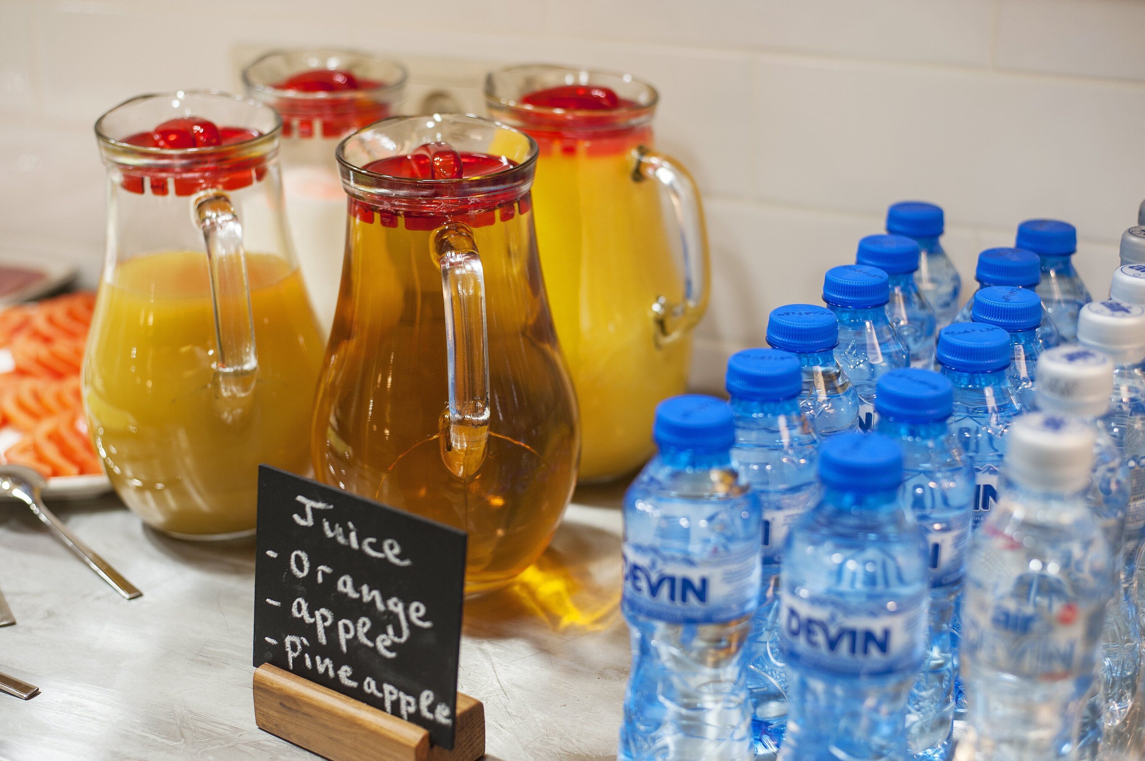 Ein Getränkeangebot mit Kännchen Orangensaft, Apfelsaft und Ananassaft sowie mehreren Wasserflaschen.