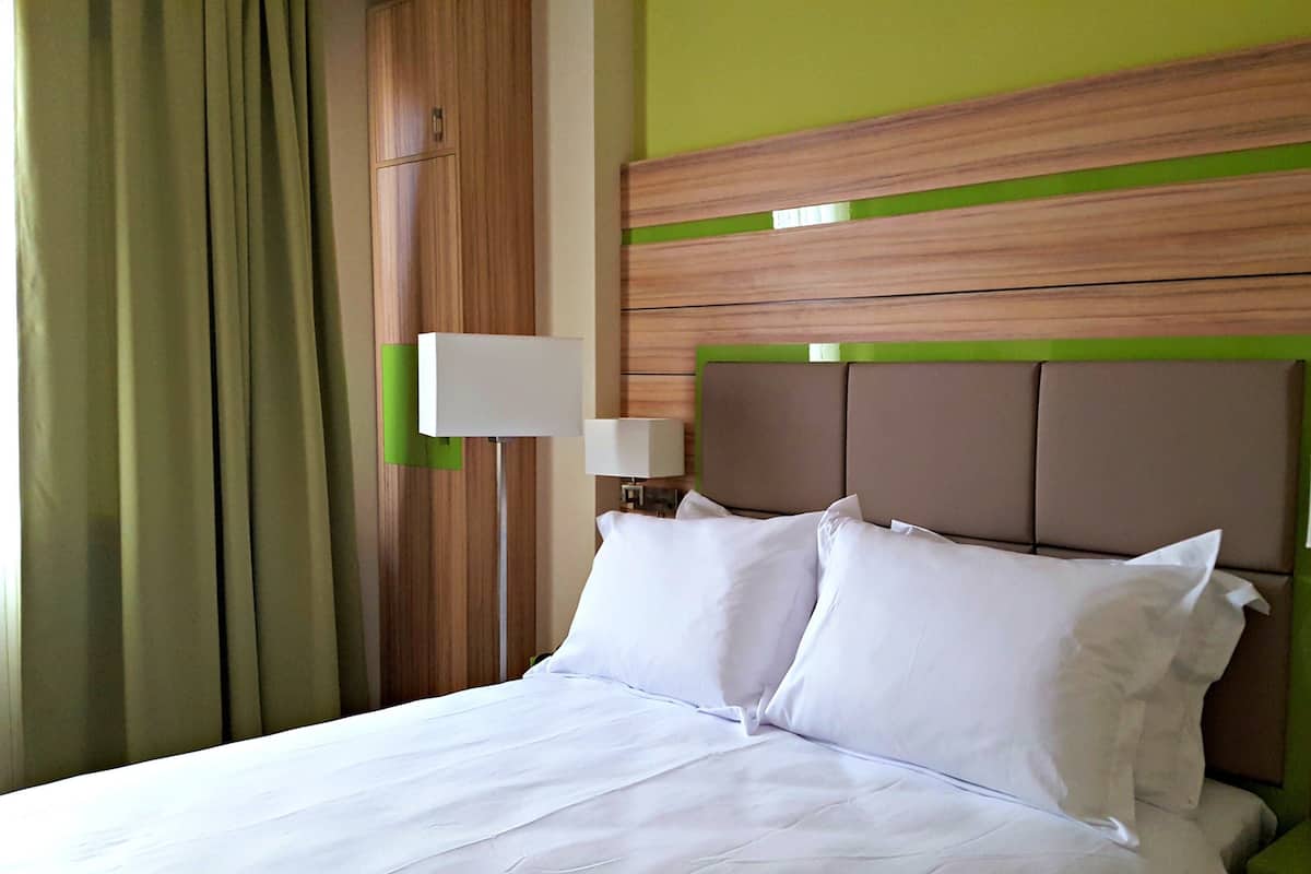 A hotel room with a bed, two bedside lamps, and a green accent wall.