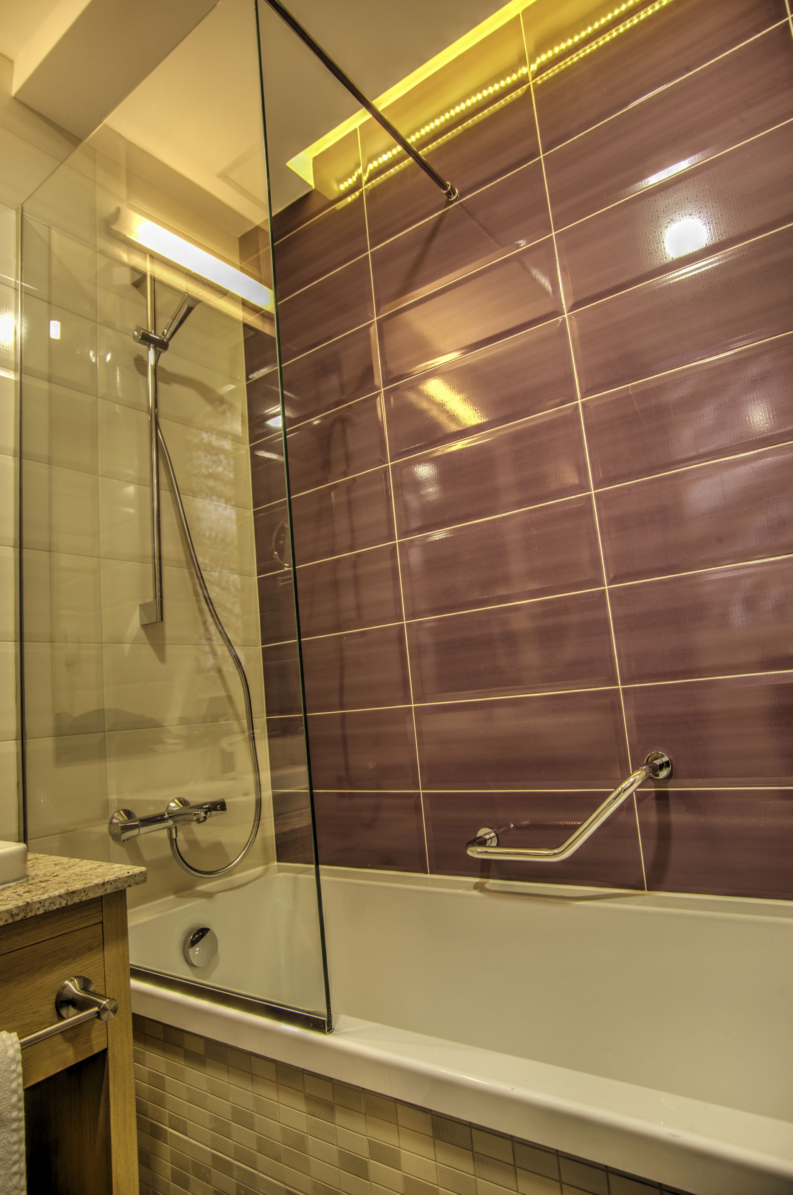 A modern bathroom with a glass-enclosed shower, a white bathtub, and a tiled wall with a grid pattern.