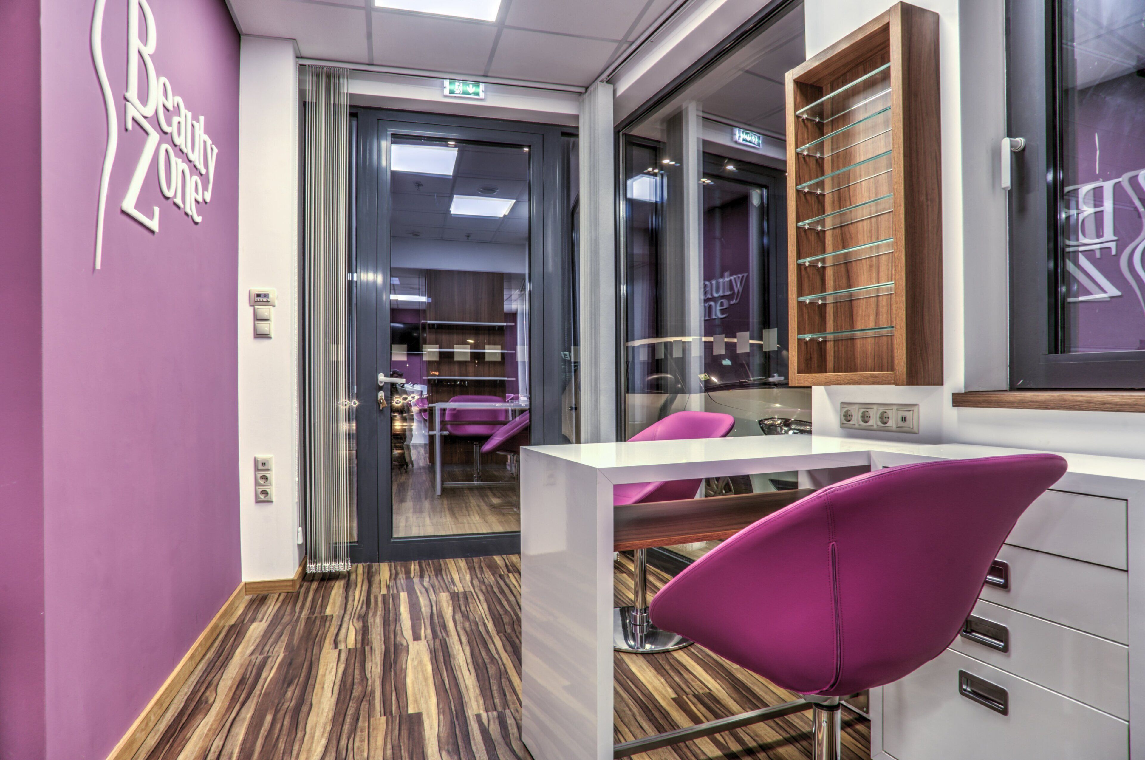 A salon interior with purple walls, a wooden floor, and modern furniture including a purple chair and a white counter.