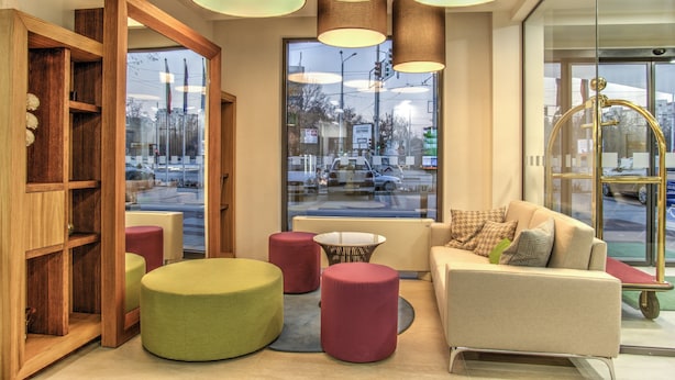 A modern interior with a sofa, ottomans, and a wooden bookshelf. - Holiday Inn Plovdiv by IHG (Plovdiv)
