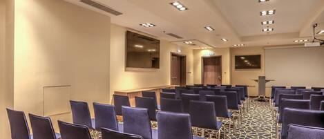 Un salón de conferencias con filas de sillas, una pantalla de proyector y un atril.
