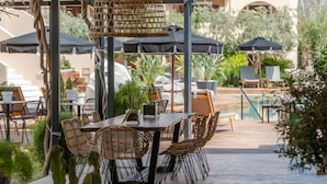 An outdoor dining area with wicker chairs and tables, surrounded by umbrellas and potted plants. - Bitzaro Palace Hotel - All inclusive (Zakynthos)