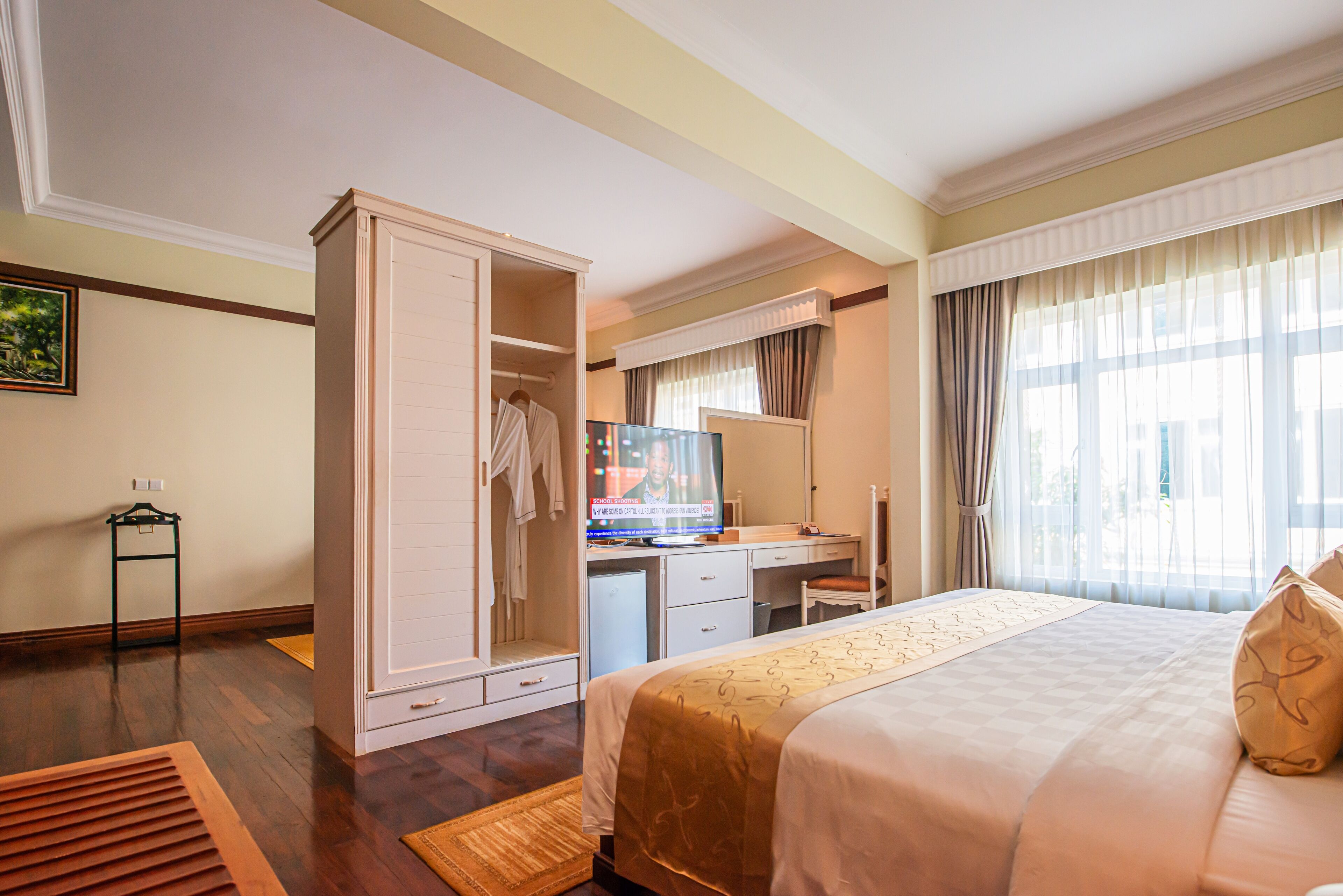Habitación de hotel con cama, escritorio, armario, televisor y ventana con cortinas.