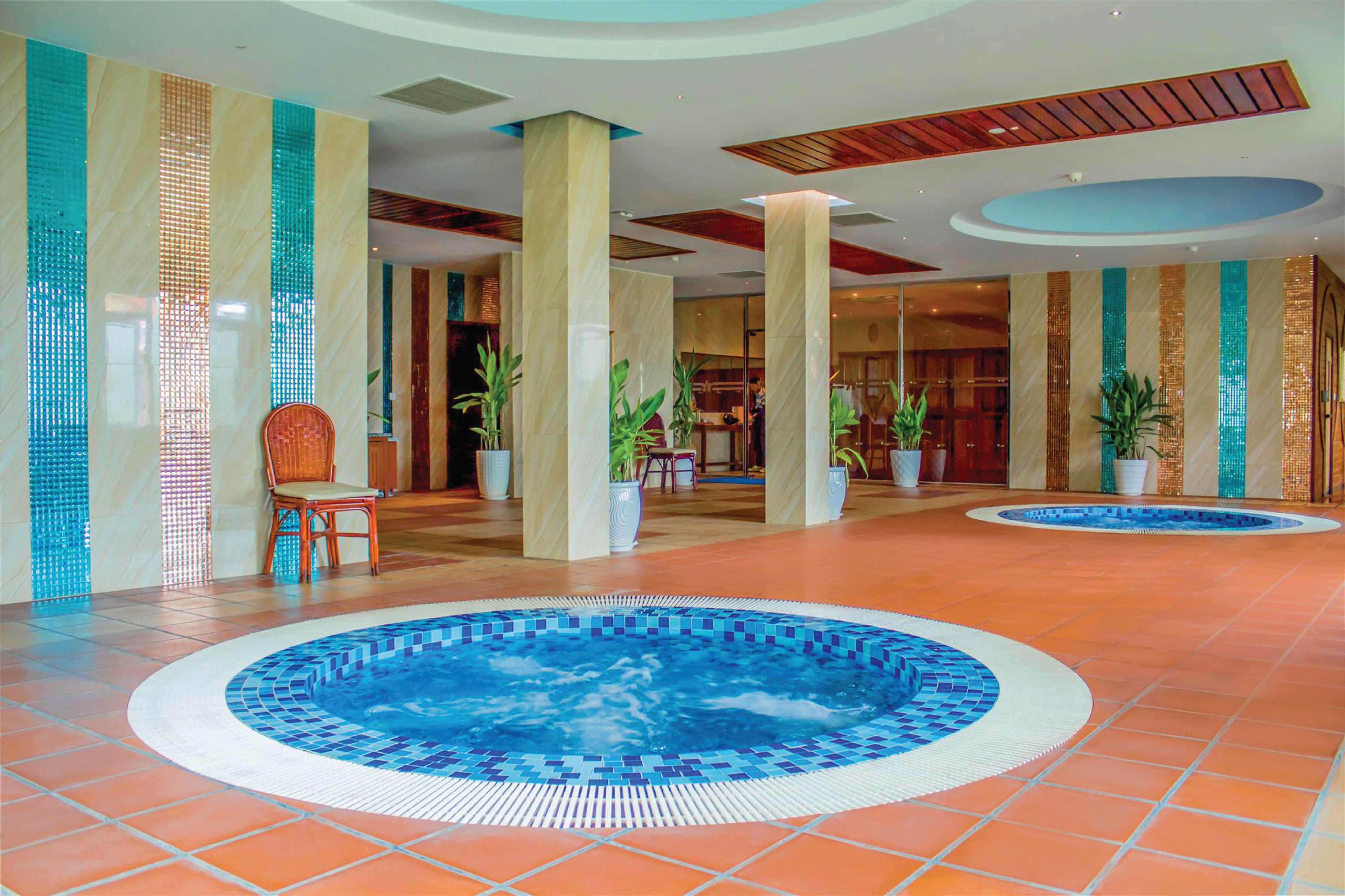A hotel lobby with a central swimming pool, large pillars, and potted plants.