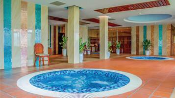 A hotel lobby with a central swimming pool, large pillars, and potted plants.