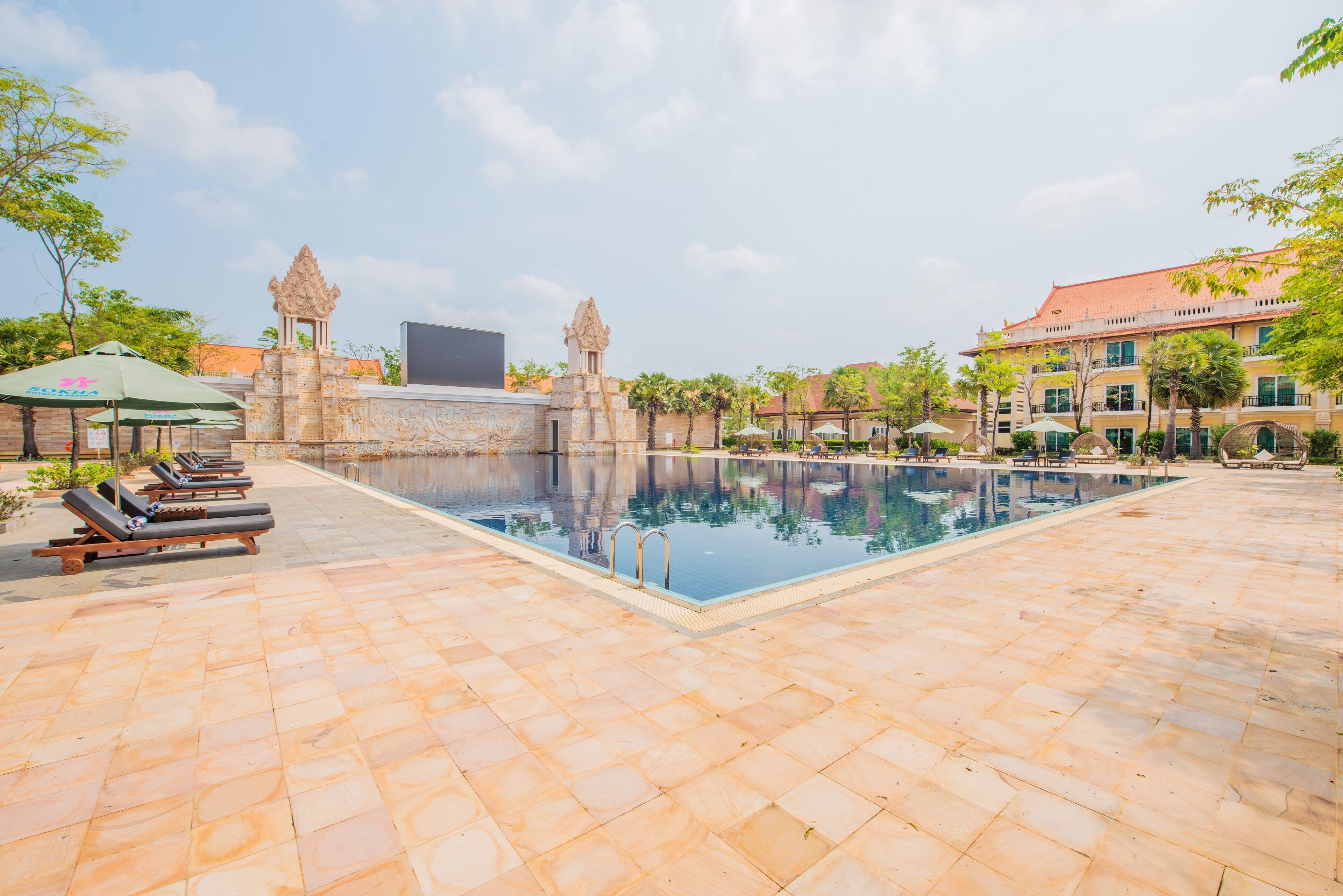 Una piscina con sillas de descanso y sombrillas, rodeada de estructuras y edificios de piedra.