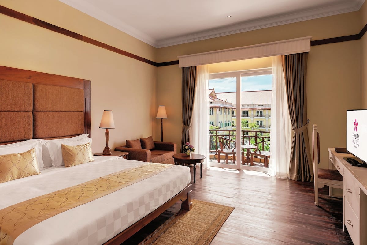 Ein Hotelzimmer mit einem großen Bett, einer Couch, einem Fernseher und einem Balkon mit Blick auf Gebäude.