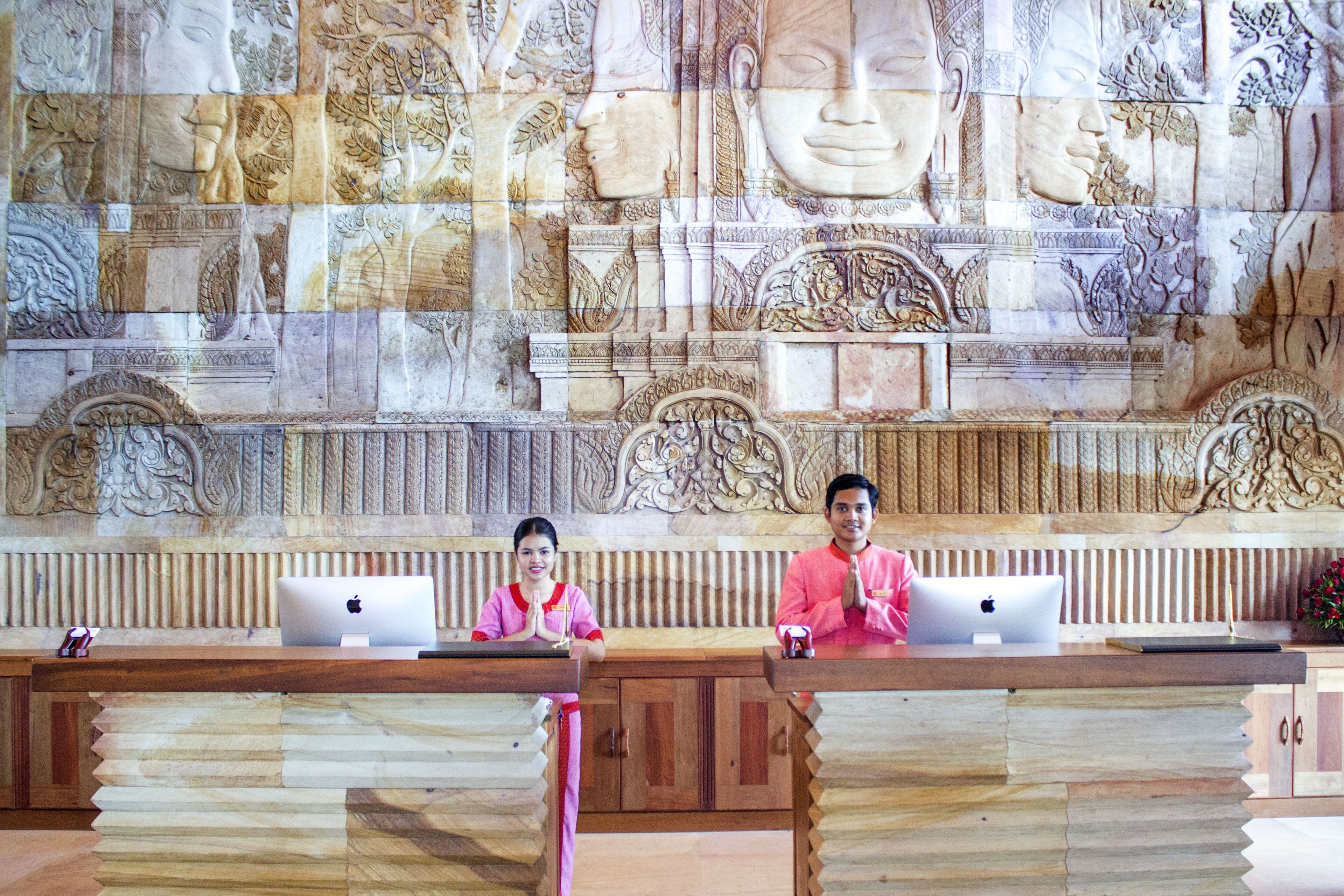 A reception desk with two staff members, a laptop, and a small statue.