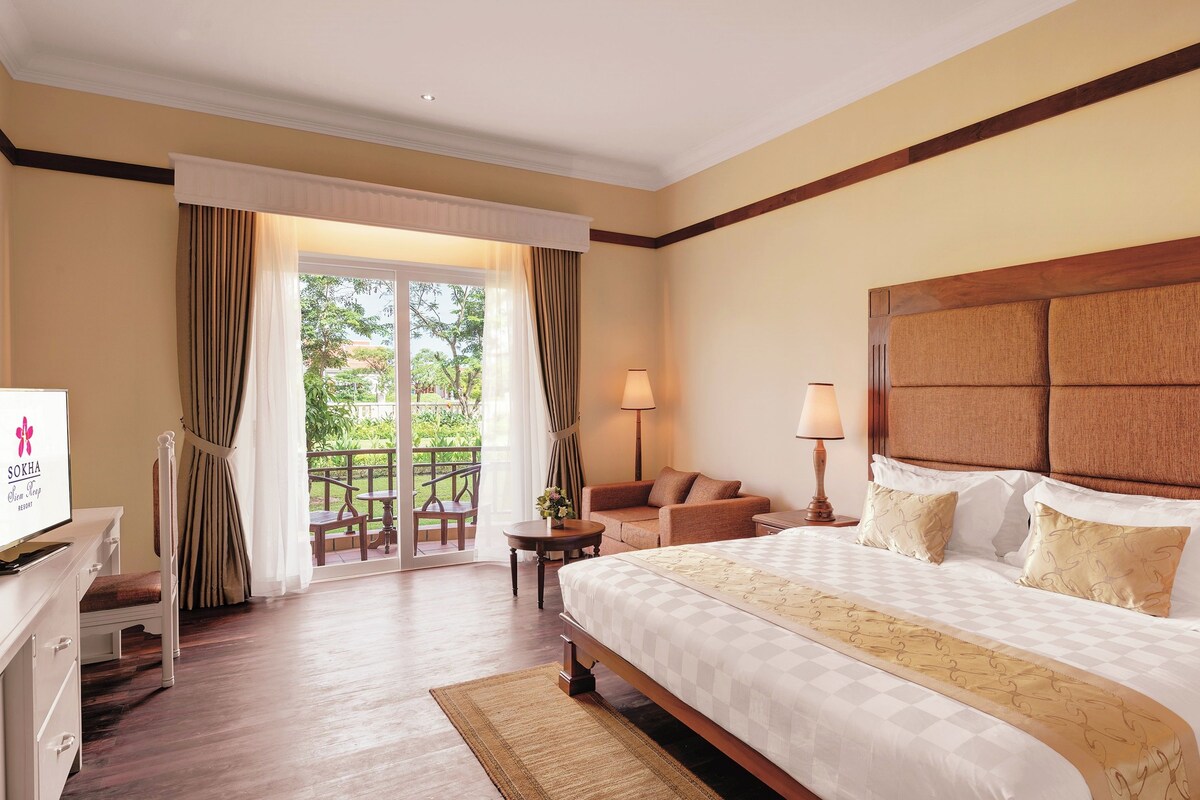 Une chambre d’hôtel avec un grand lit, un bureau, une chaise, un canapé et un balcon avec des rideaux.
