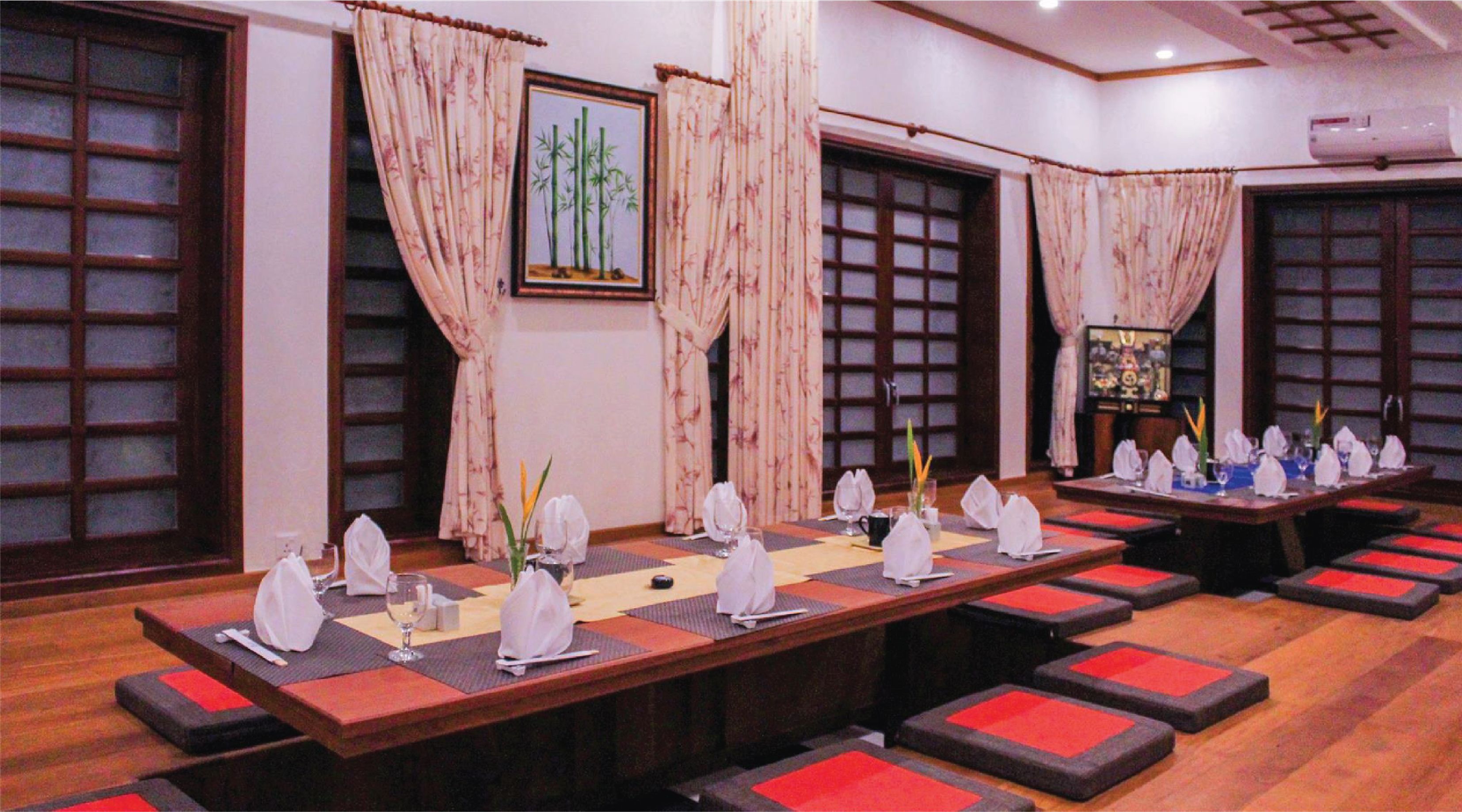 Une salle de conférence avec une longue table préparée pour une réunion, de grandes fenêtres ornées de rideaux classiques et un tableau représentant des bambous, encadré et accroché au mur.