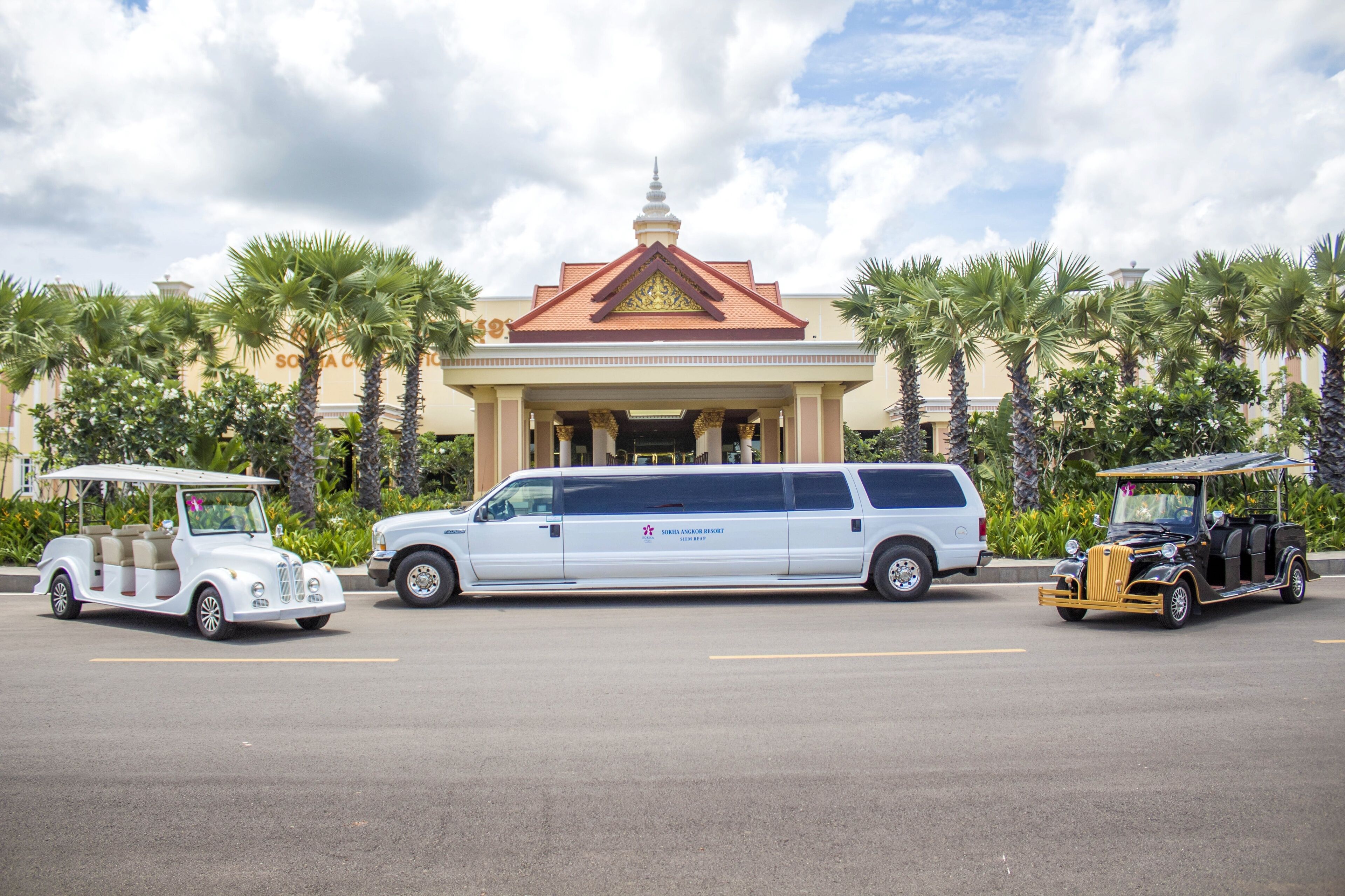 A white minivan parked in front of a building with a traditional architectural style, palm trees, and a clear sky.