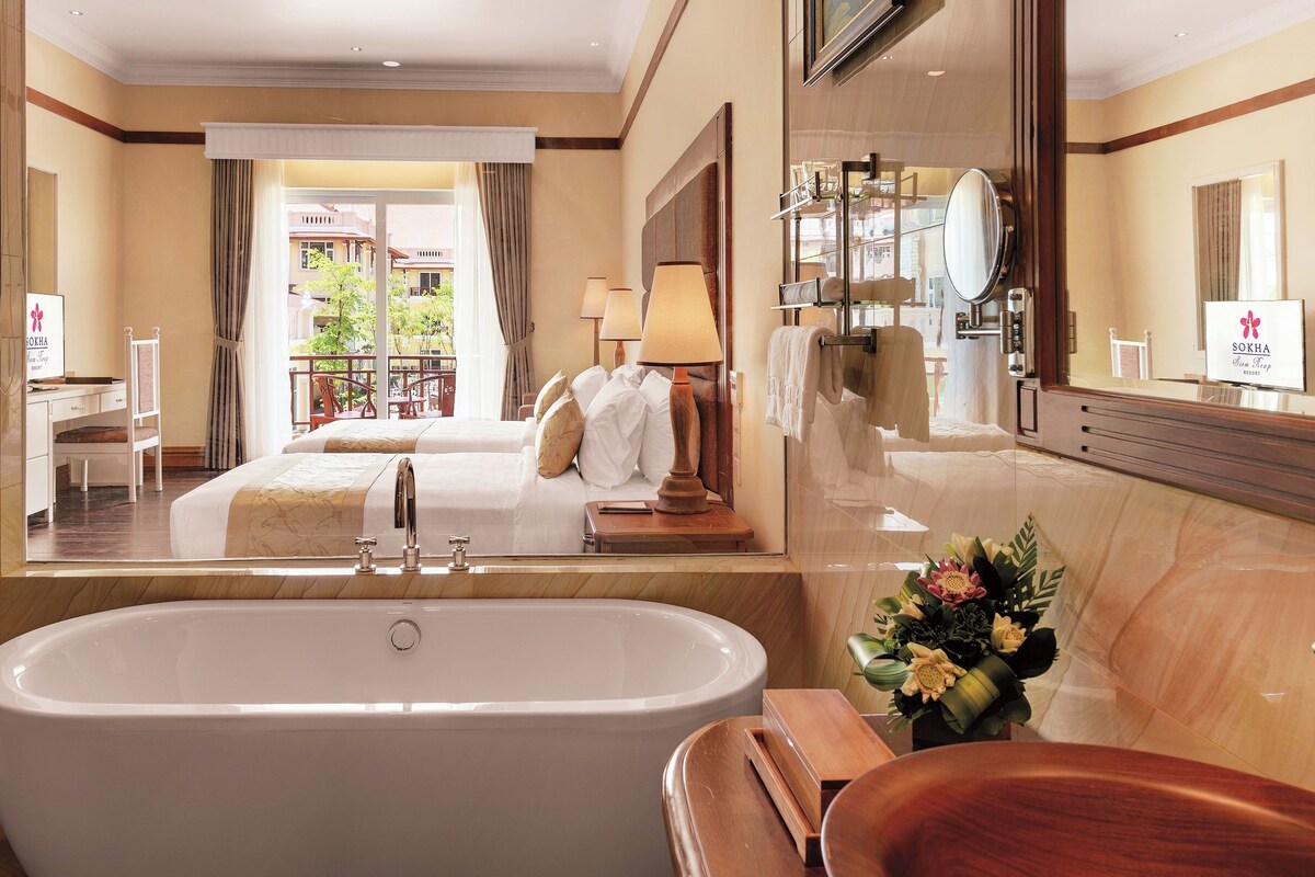 Une salle de bain d’hôtel avec une grande baignoire, un meuble-lavabo en bois et un miroir.