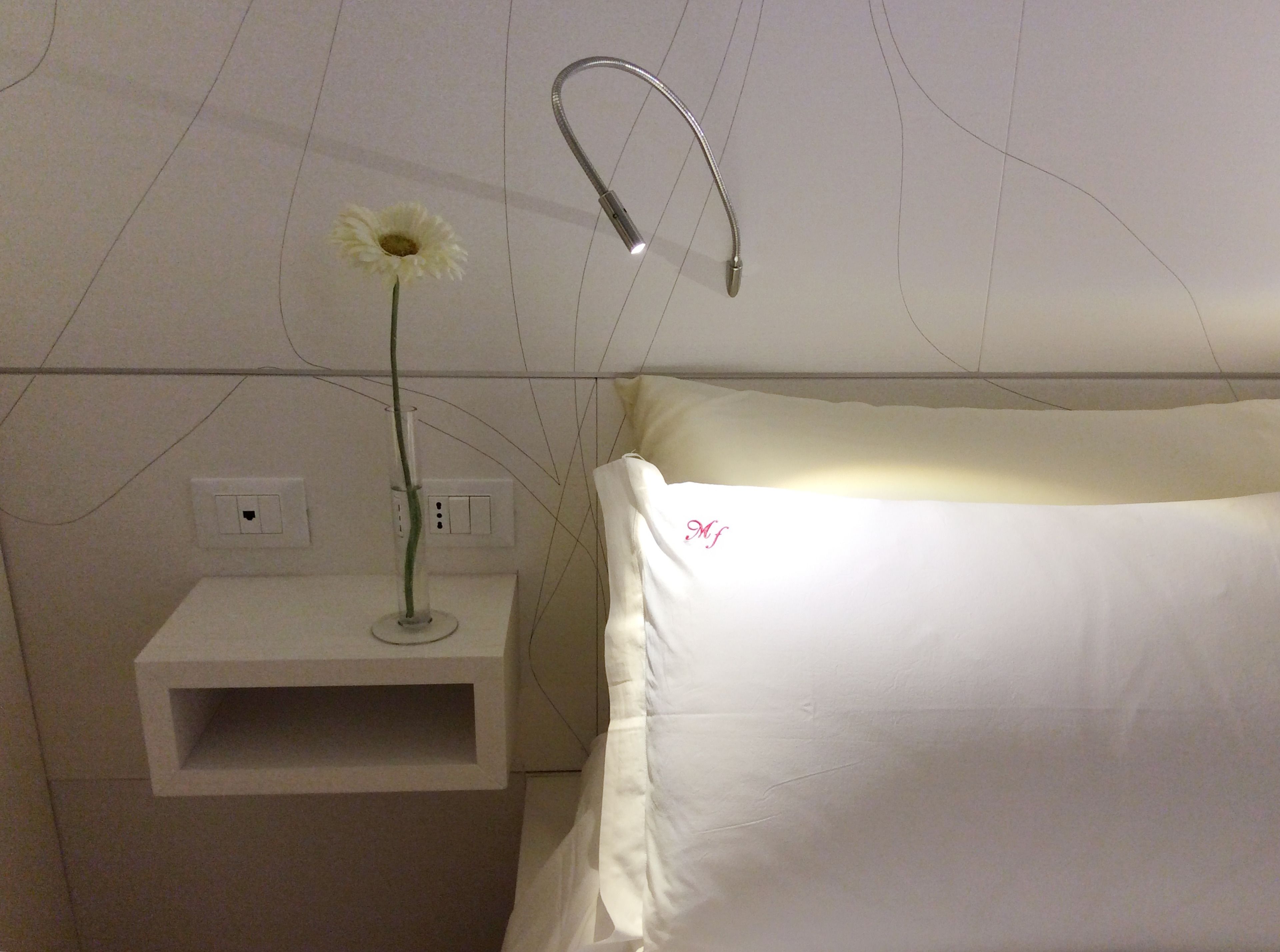 Una mesita de noche blanca con una única florera, un enchufe y un interruptor.