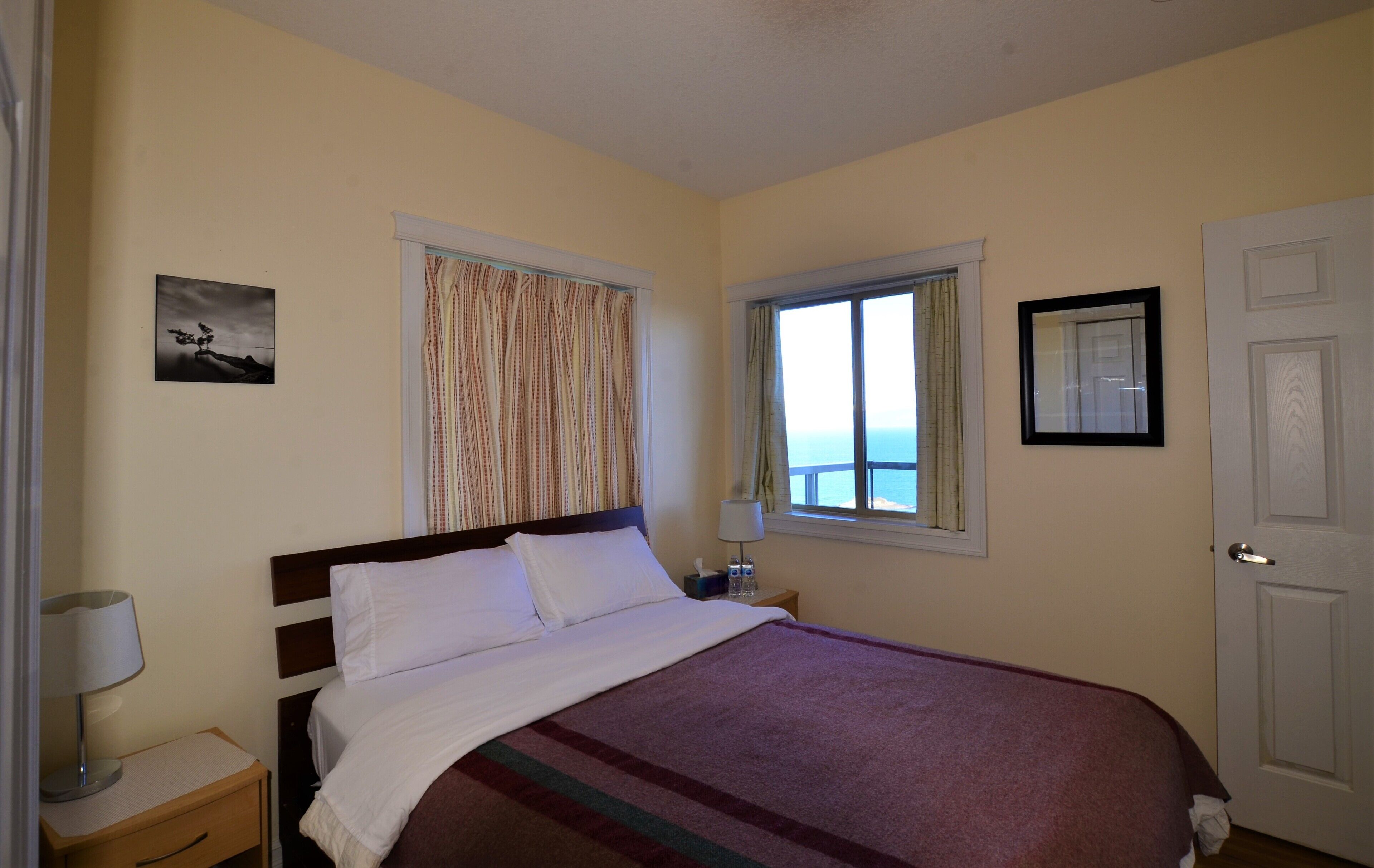 Un dormitorio con cama, mesita de noche, lámpara, ventana con cortinas y puerta.
