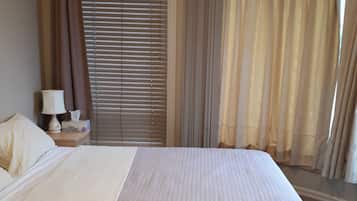 Habitación de hotel con una cama grande, una mesita de noche con lámpara y una ventana con cortinas.